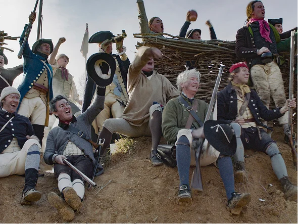 Group of people in historical military uniforms cheering outdoors.