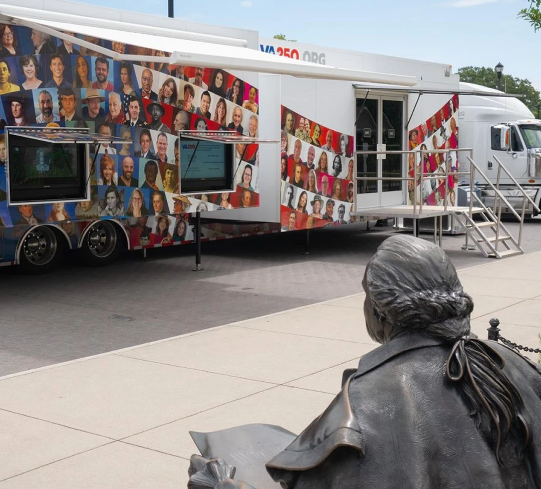 A large trailer with a collage of portraits and interactive screens, next to a bronze statue.